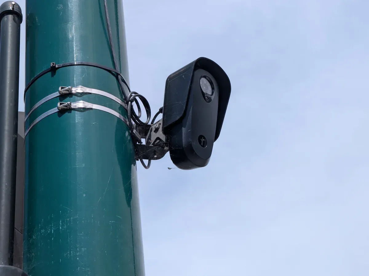 Close view of a black Flock Safety license-plate-reader camera attached to a green roadside pole.