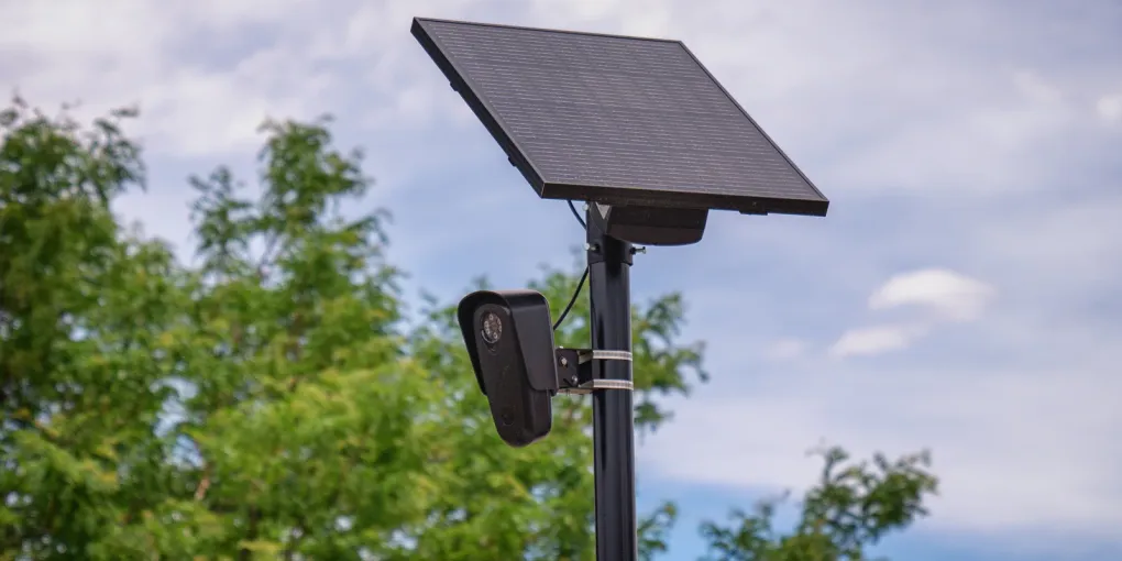 A Flock Safety automated license-plate-reader camera mounted below a solar panel on a roadside pole.